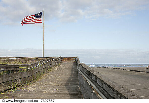 Boardwalk through grassland with mountains and American flag flying.