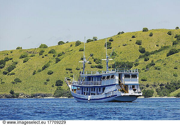 Boat moored in blue water and tree hillside along the shoreline  Komodo National Park; East Nusa Tenggara  Indonesia