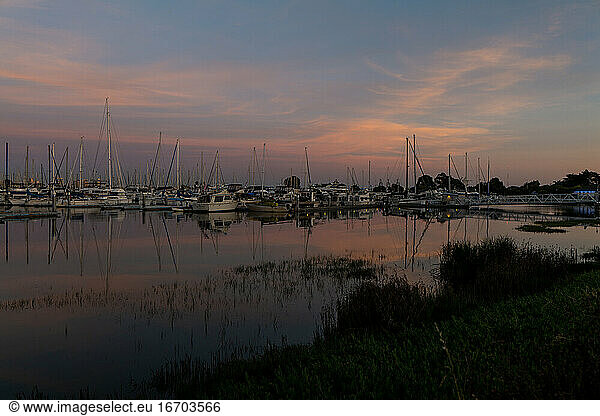 Boats in harbor during sunset with colorful sky reflecting in water