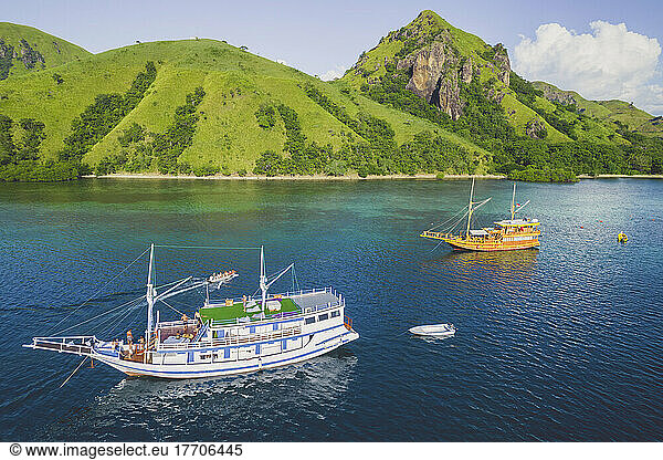 Boats in the tranquil waters along the lush and rugged coastline of Komodo National Park; East Nusa Tenggara  Indonesia