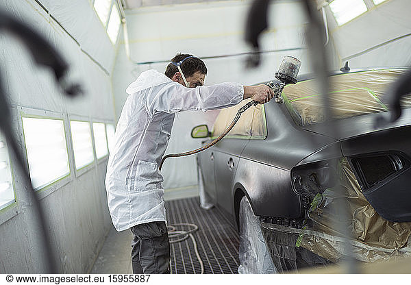 Body painter painting car in paint booth