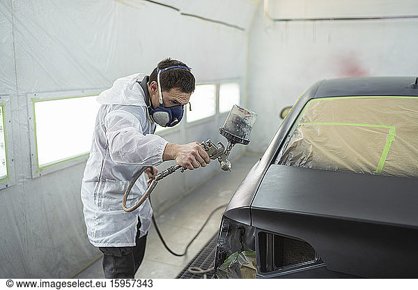 Body painter painting car in paint booth