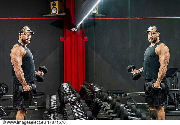 Bodybuilder exercising with dumbbells standing in gym
