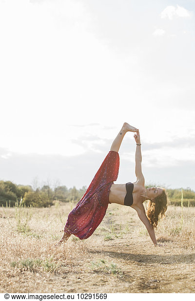 Boho woman in extended side plank yoga pose in sunny rural field