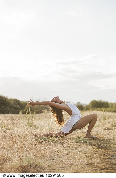 Boho woman in high crescent lunge yoga pose in sunny rural field