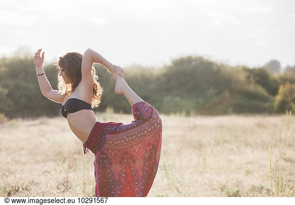 Boho woman in king dancer yoga pose in sunny rural field