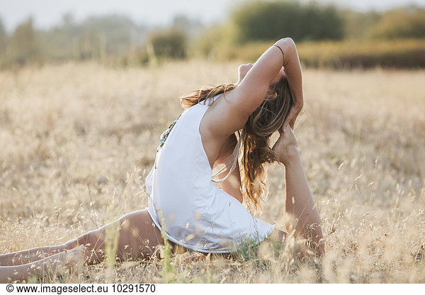 Boho woman in royal king pigeon pose in sunny rural field