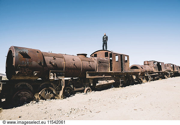 Bolivien  Uyuni-Zugfriedhof  Mann auf der Kabine eines alten rostigen Zuges stehend