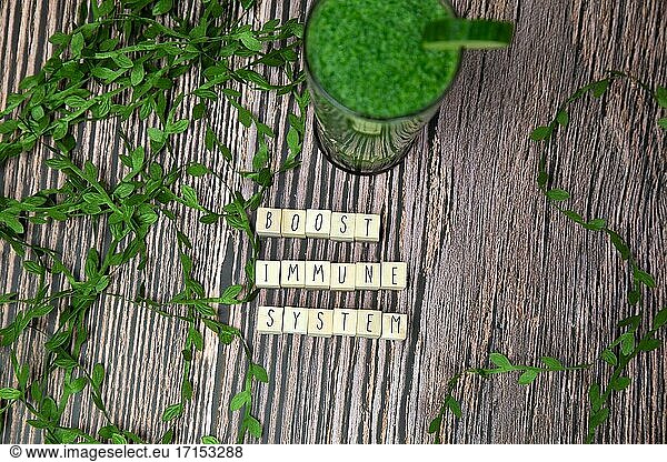 Boost your immune system - inspirational text on a wooden background texture with a glass of fresh green  vegetable juice  healthy lifestyle and wellbeing concept modern design.