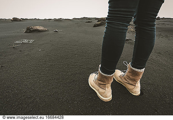 Boots of young female in black sand near Reynisfjara beach in Iceland