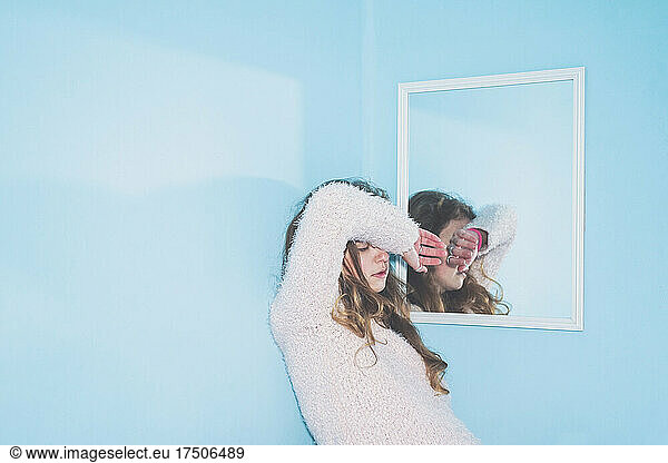Bored woman with hand on head leaning by mirror at home