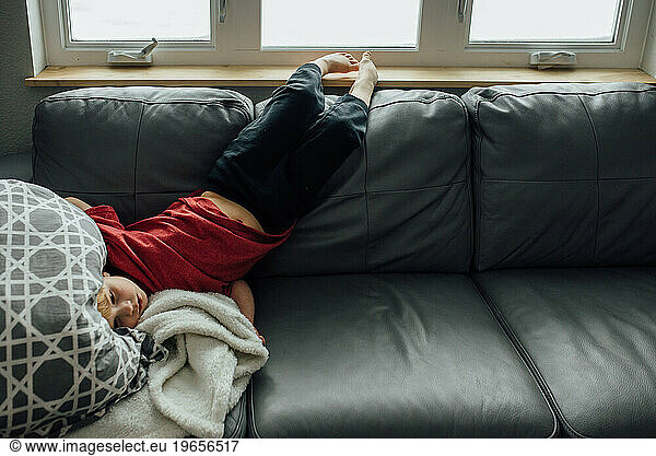 Bored young boy lays upside down over back of couch with head on