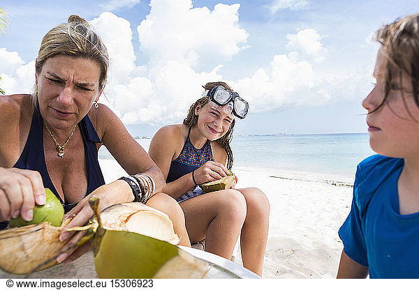 Bother and her kids cutting a coconut on a sandy beach