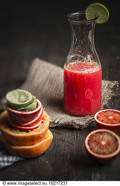 Bottle of juice with blood oranges on table  close up