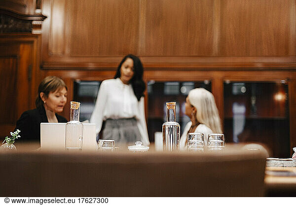 Bottles and glasses on table while female financial advisors in background at workplace