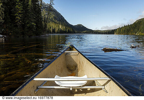 Bow of a canoe a secluded lake surrounded by forest  mountains and sky