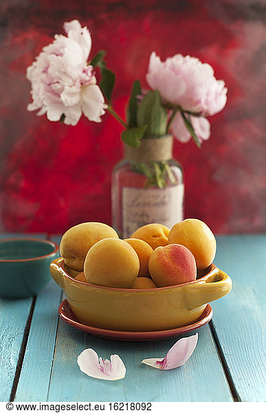 Bowl of apricots with peonies flowers on wooden table