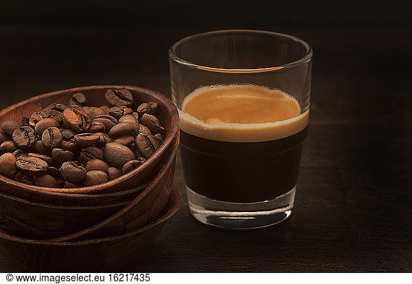 Bowl of coffee beans and espresso against black background  close up
