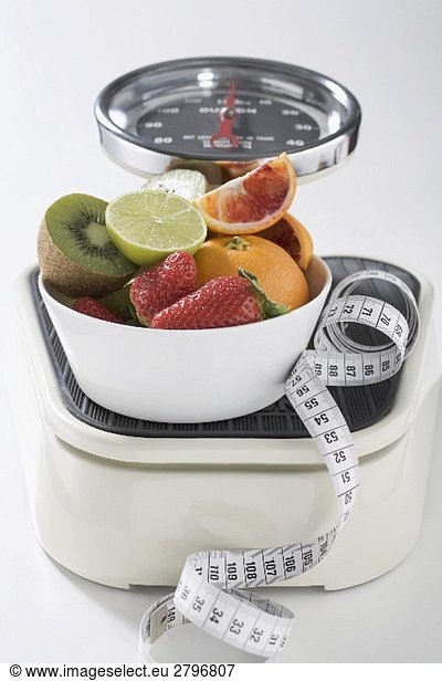 Bowl of fresh fruit and tape measure on scales