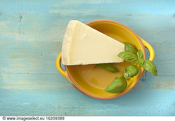 Bowl of parmesan cheese with basil on wooden table  close up
