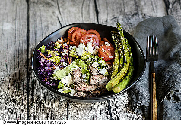Bowl of salad with steak  asparagus  tomatoes  shredded red cabbage  lettuce and feta cheese