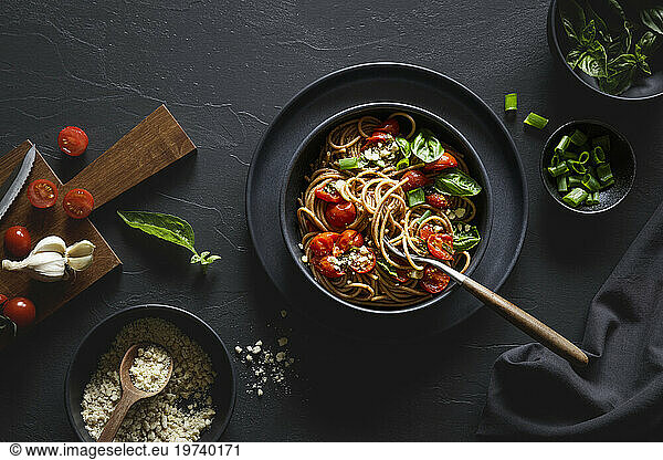 Bowl of vegan wholemeal spelt spaghetti with tomatoes  basil  scallion and cashew Parmesan