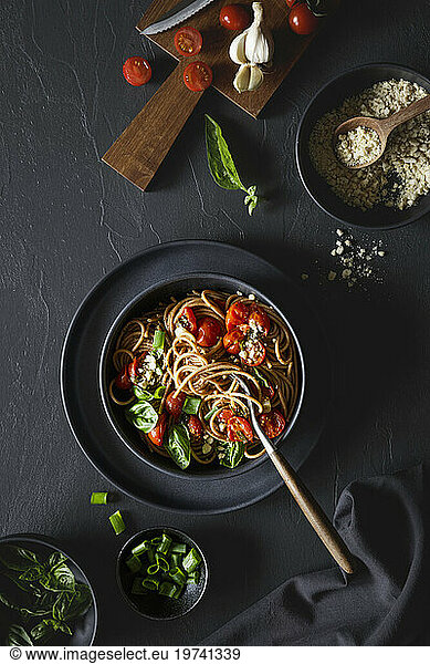Bowl of vegan wholemeal spelt spaghetti with tomatoes  basil  scallion and cashew Parmesan