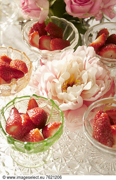 Bowls of strawberries and flowers on table