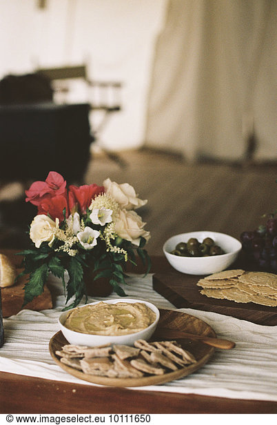Bowls with hummus and olives and a vase of flowers on a table.