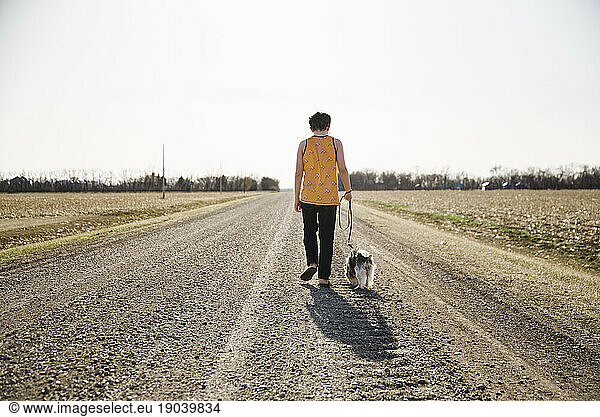 Boy and dog walking on a road in the country with a clear sky.