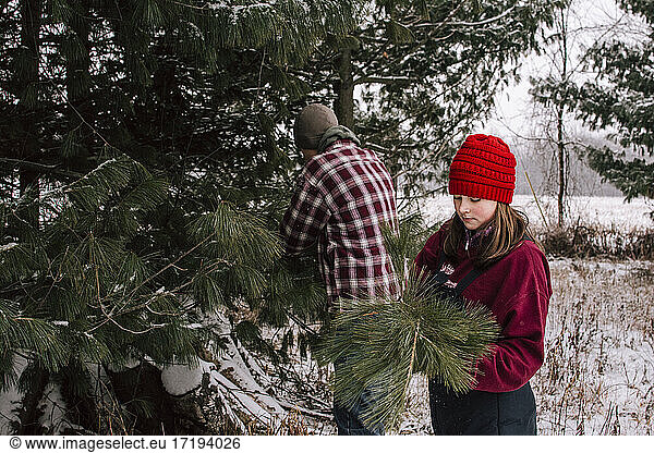 Boy and Girl in Winter Clothing Clipping Pine Branches for Christmas