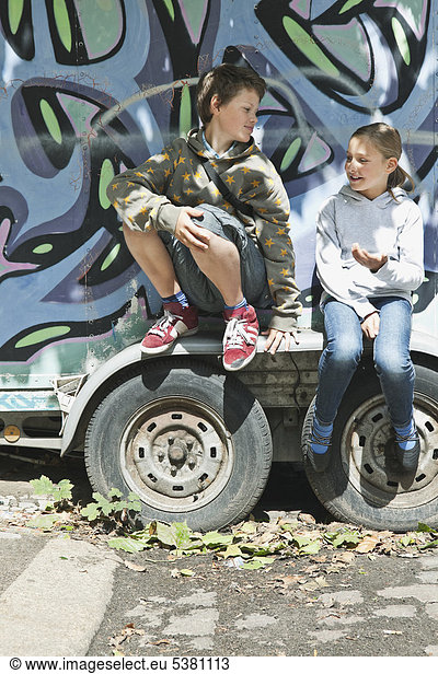 Boy and girl sitting on graffiti truck