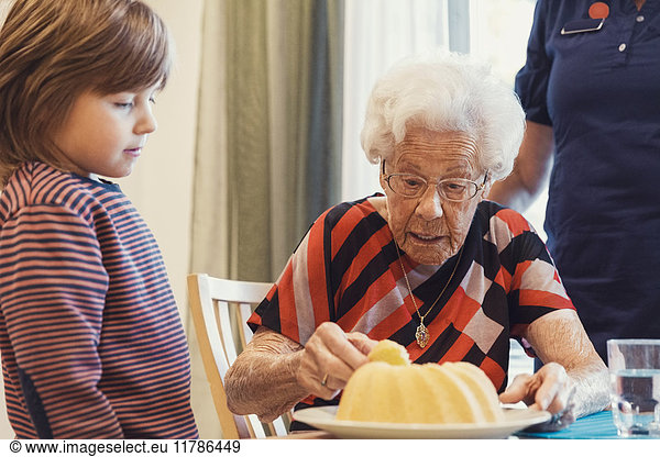 Boy and great grandmother looking at sponge cake in house