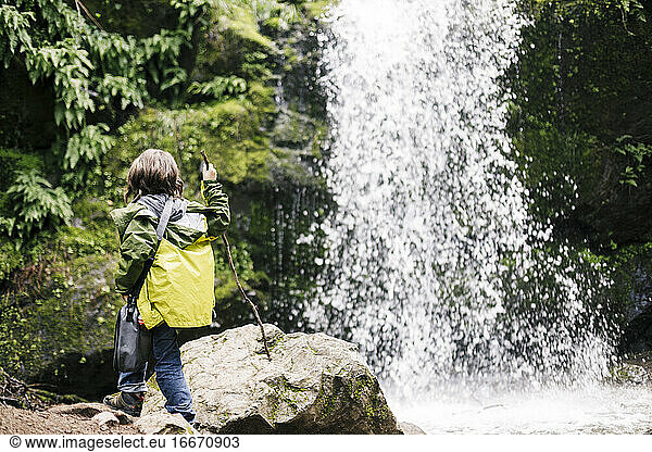 Boy at the end of hiking standing looking waterfall at green forest