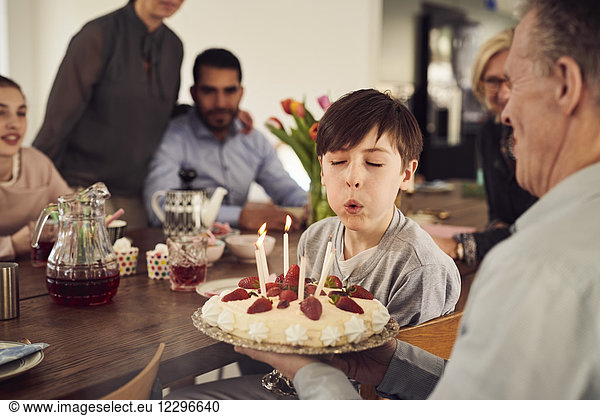 Boy blowing candles on birthday cake while enjoying in party with family at home