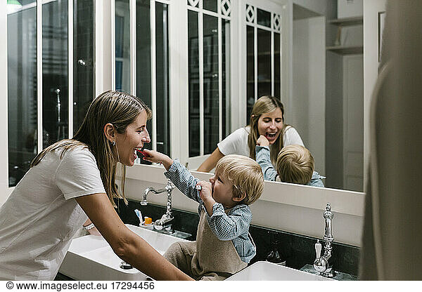 Boy brushing mother's teeth in bathroom at home