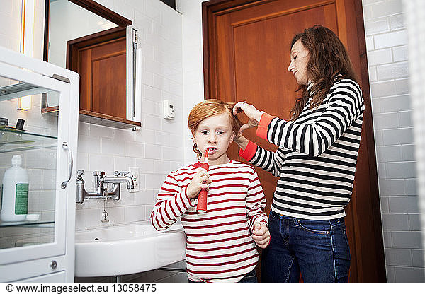 Boy brushing teeth while mother combing hair in bathroom
