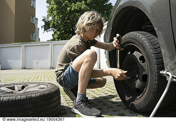 Boy changing car tire in yard