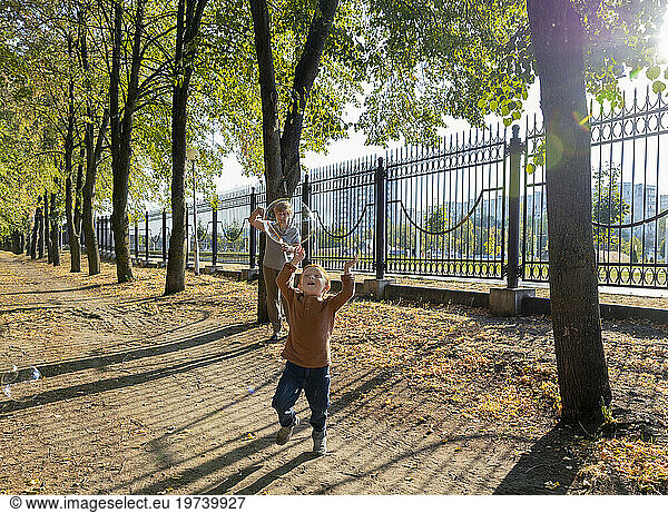 Boy chasing soap bubbles with grandmother in background at autumn park