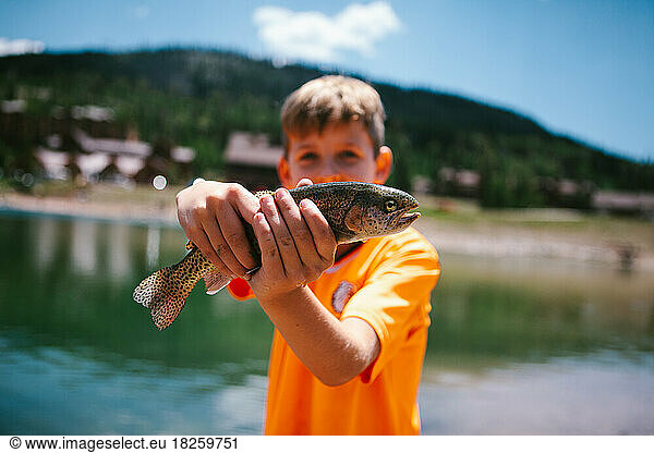 Boy child hold fish he caught fishing by mountain pond