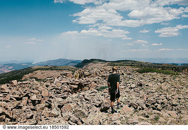 Boy climbing on rocky ground with blue sky in mountain range