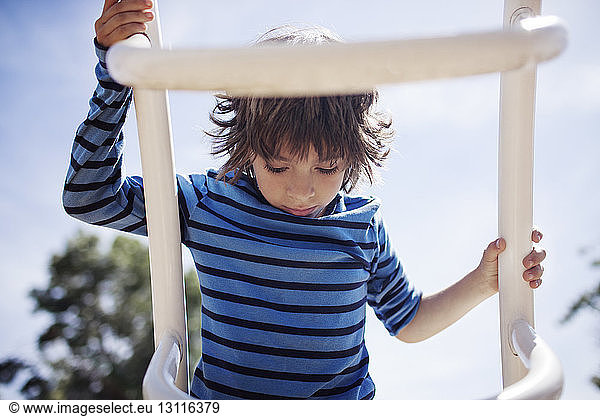 Boy climbing outdoor play equipment against sky