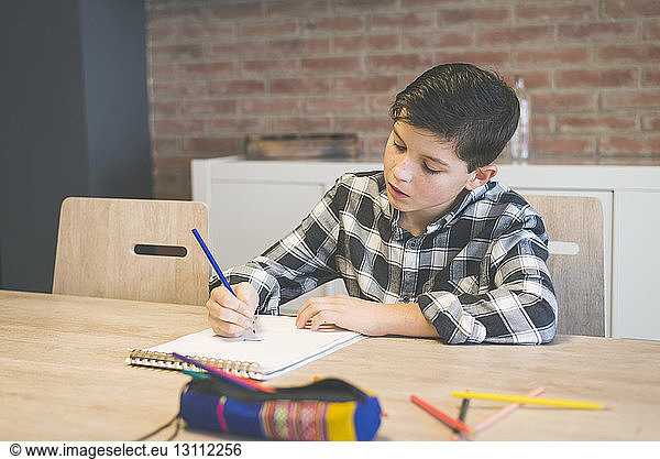 Boy coloring on spiral notebook with colored pencil at table in home
