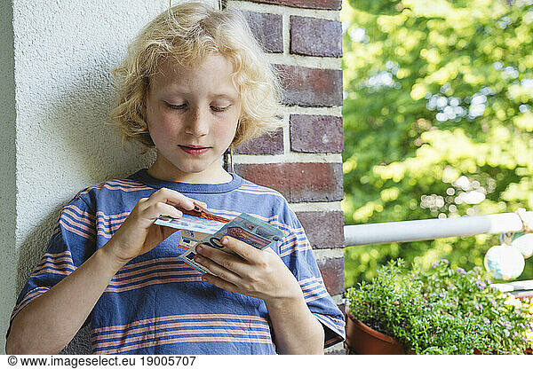 Boy counting euro notes leaning on wall