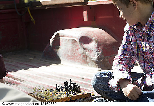 Boy cross legged in back of pickup truck playing chess