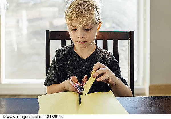 Boy cutting paper with safety scissors at home