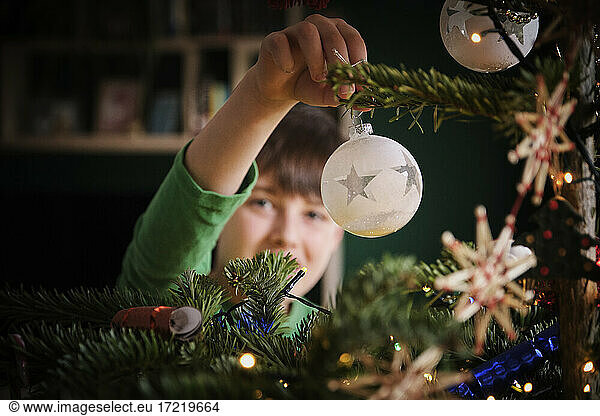 Boy decorating Christmas tree with ornaments at home