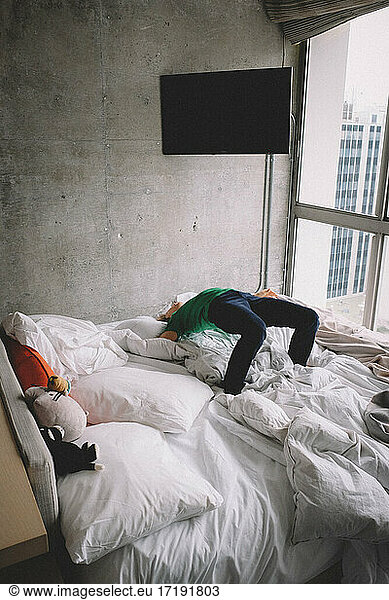 Boy does back bend on bed in modern hotel room