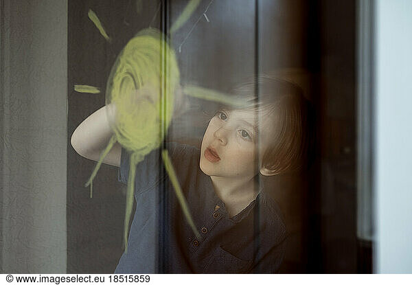 Boy drawing sun on glass