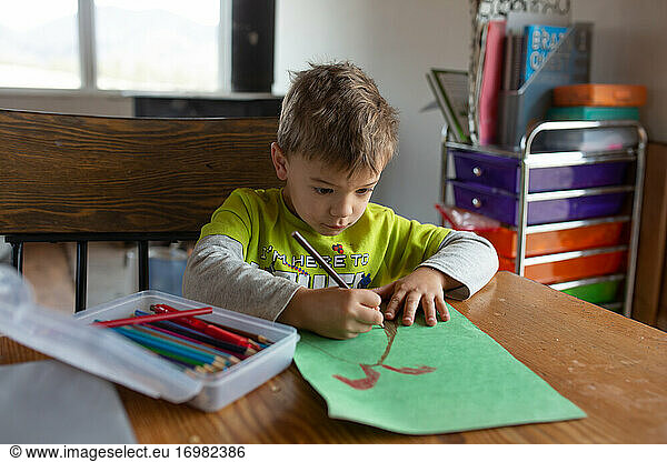 Boy drawing volcano at home table for school